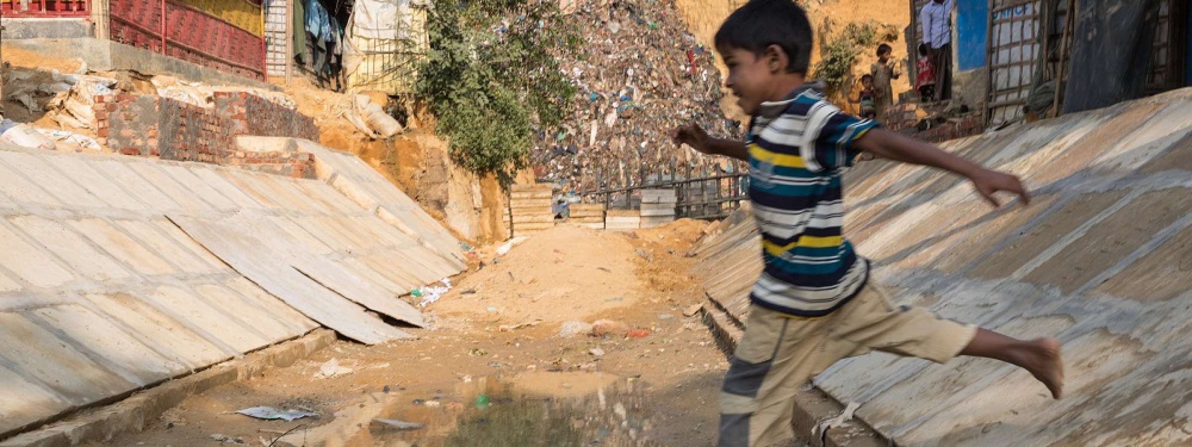 Child leaps over a drain in a camp in Bangladesh