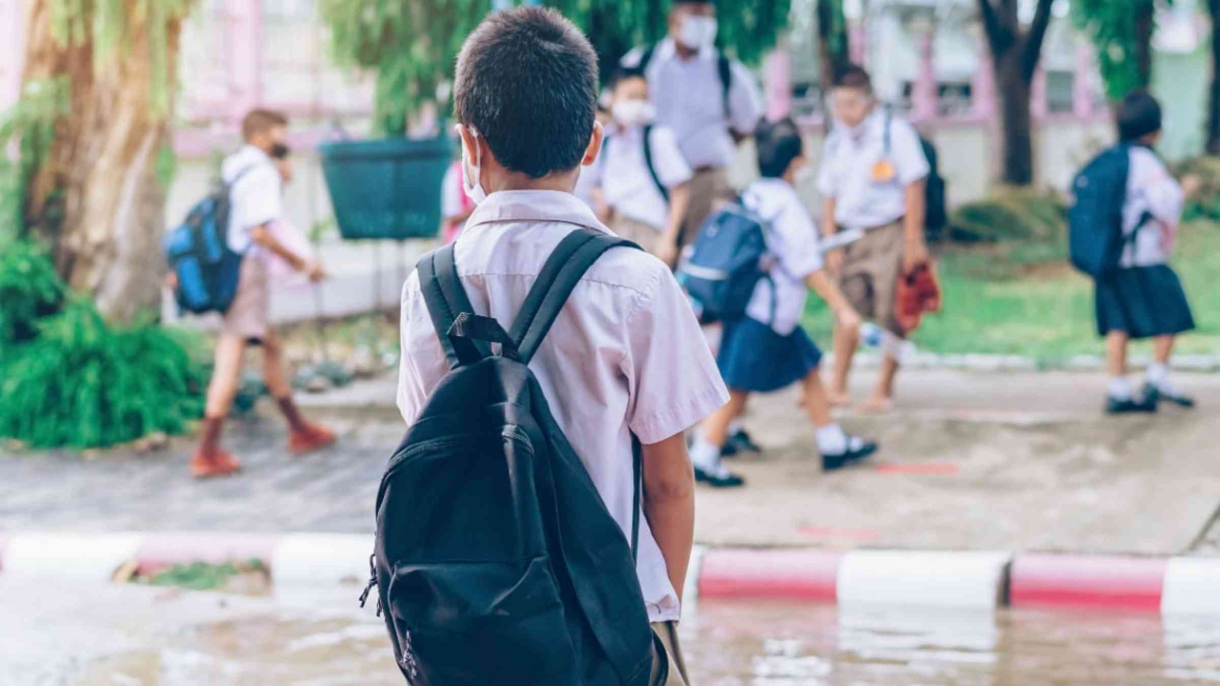 A boy dressed in his school uniform is walking though his flooded school ground.