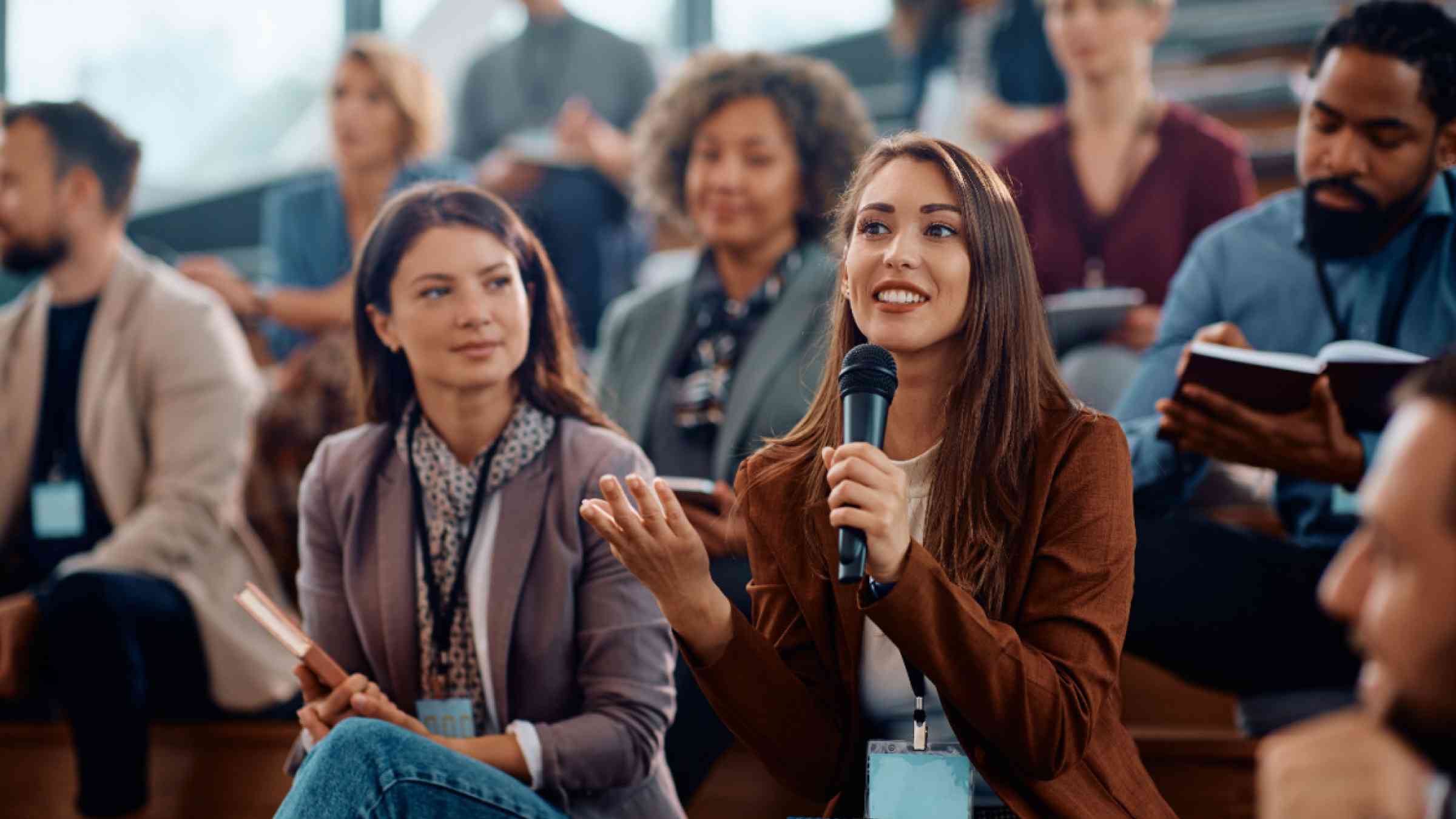 Happy female manager asking a question from the audience while participating in business seminar at convention center.