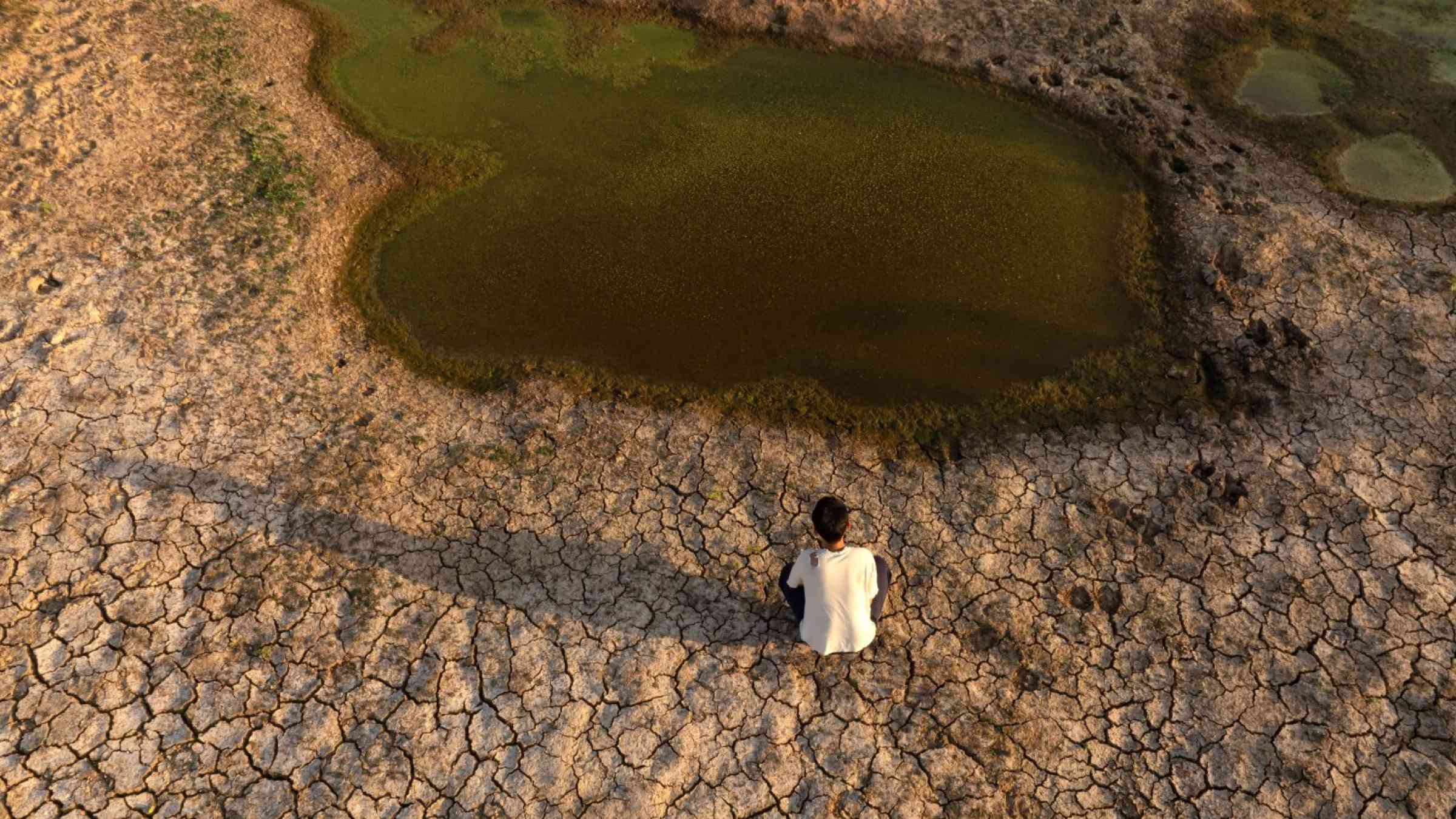 A man sits near a drying river.